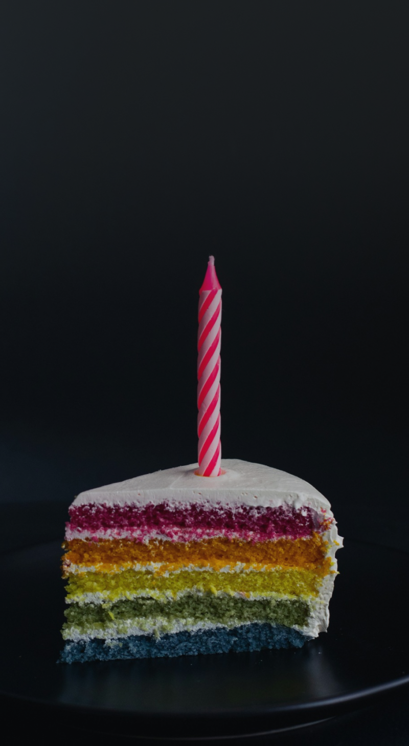 Foto de um bolo colorido com uma vela de aniversário em cima